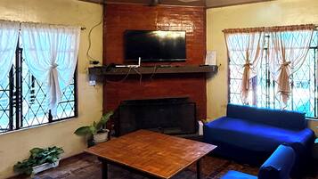 A living room with a television mounted on a wooden wall, a coffee table, blue sofas, and a chandelier.
