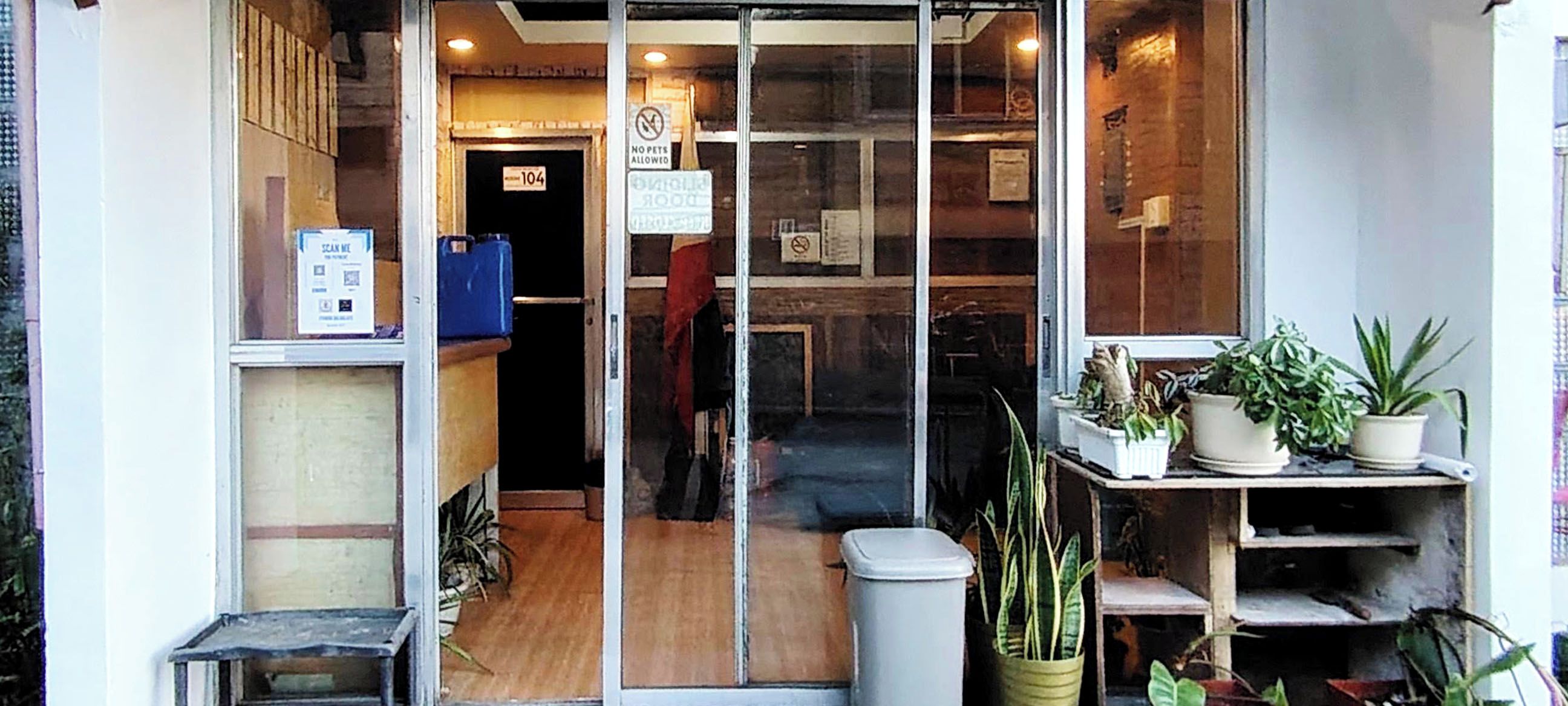 A storefront with a glass door, a 'No Pets Allowed' sign, and potted plants on the right.