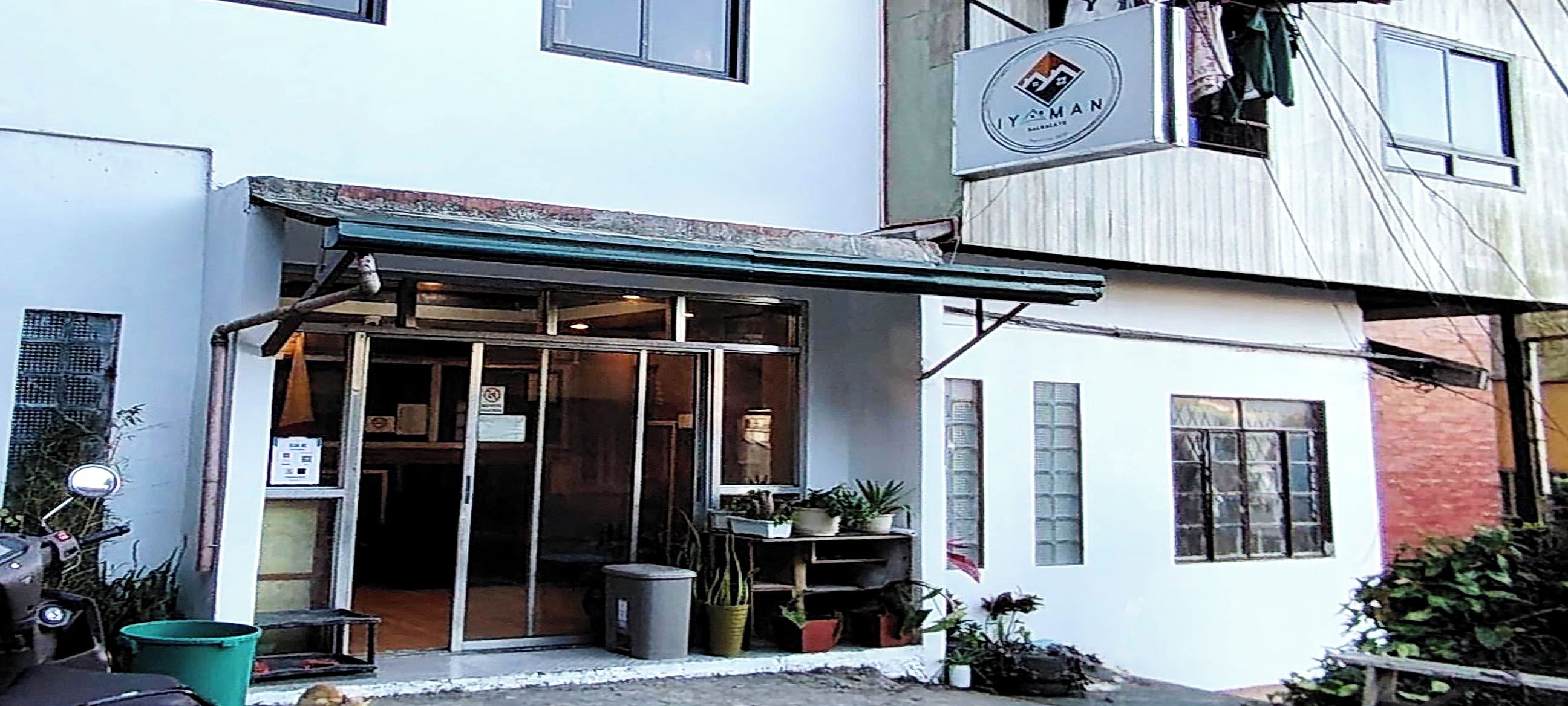 A building with a storefront, a sign above the entrance, and a small outdoor area with plants.