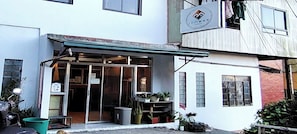 Edifício com fachada, uma placa sobre a entrada e uma pequena área externa com plantas.