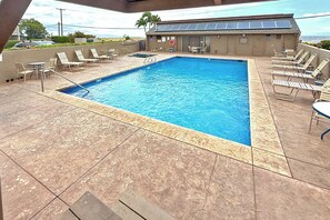 Ein rechteckiger Pool mit einer gefliesten Liegefläche, umgeben von Liegestühlen und einem Gebäude mit Solaranlage.