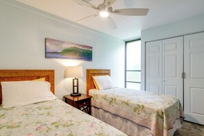 Ein Hotelzimmer mit zwei Betten, einem Deckenventilator, einem Gemälde und einem Fenster.