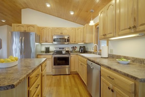 A modern kitchen with wooden cabinets, stainless steel appliances, granite countertops, and a wooden floor.
