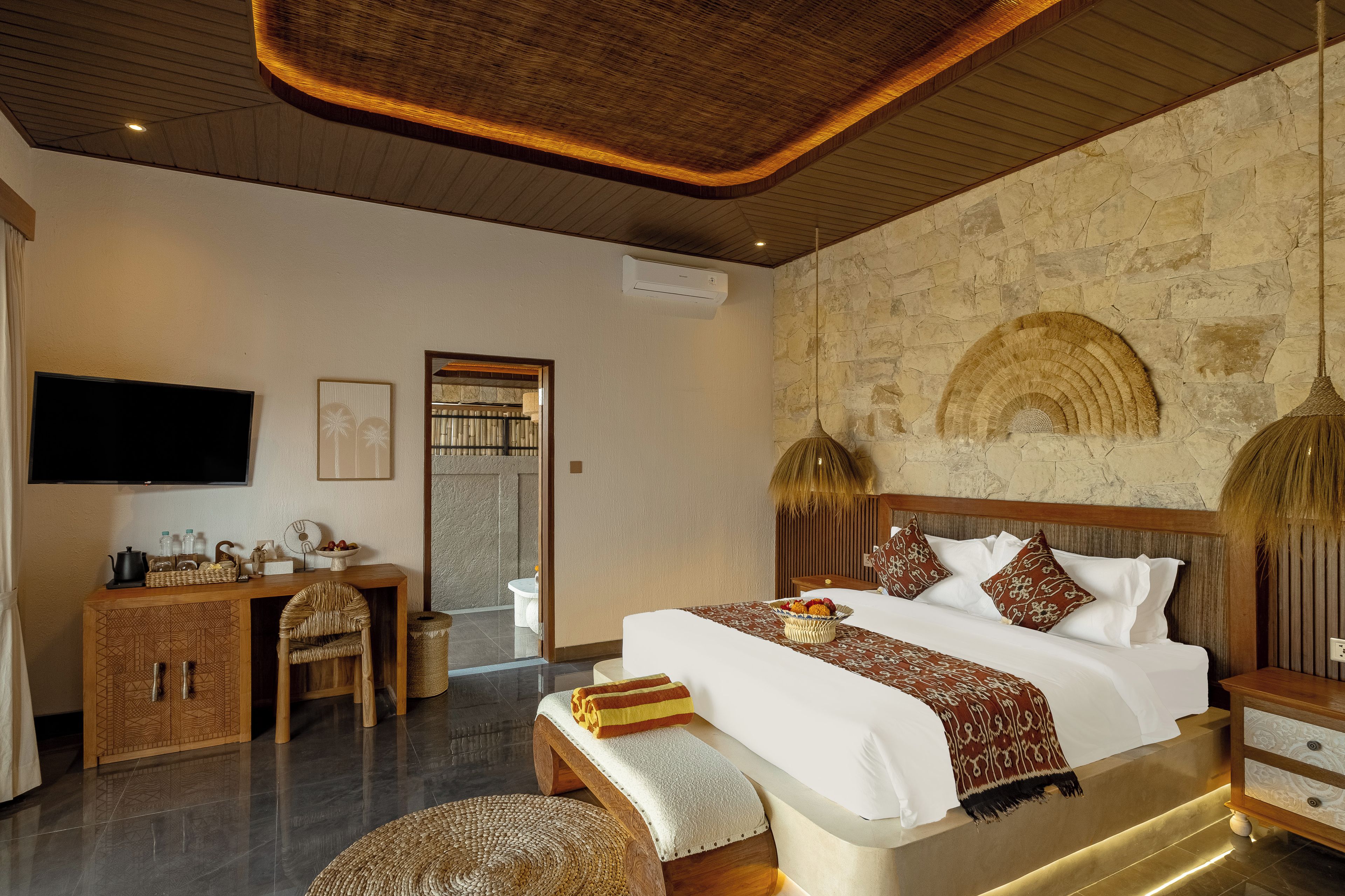 A hotel room with a bed, bedside tables, a TV, a desk with a chair, and a bathroom visible through an open door.