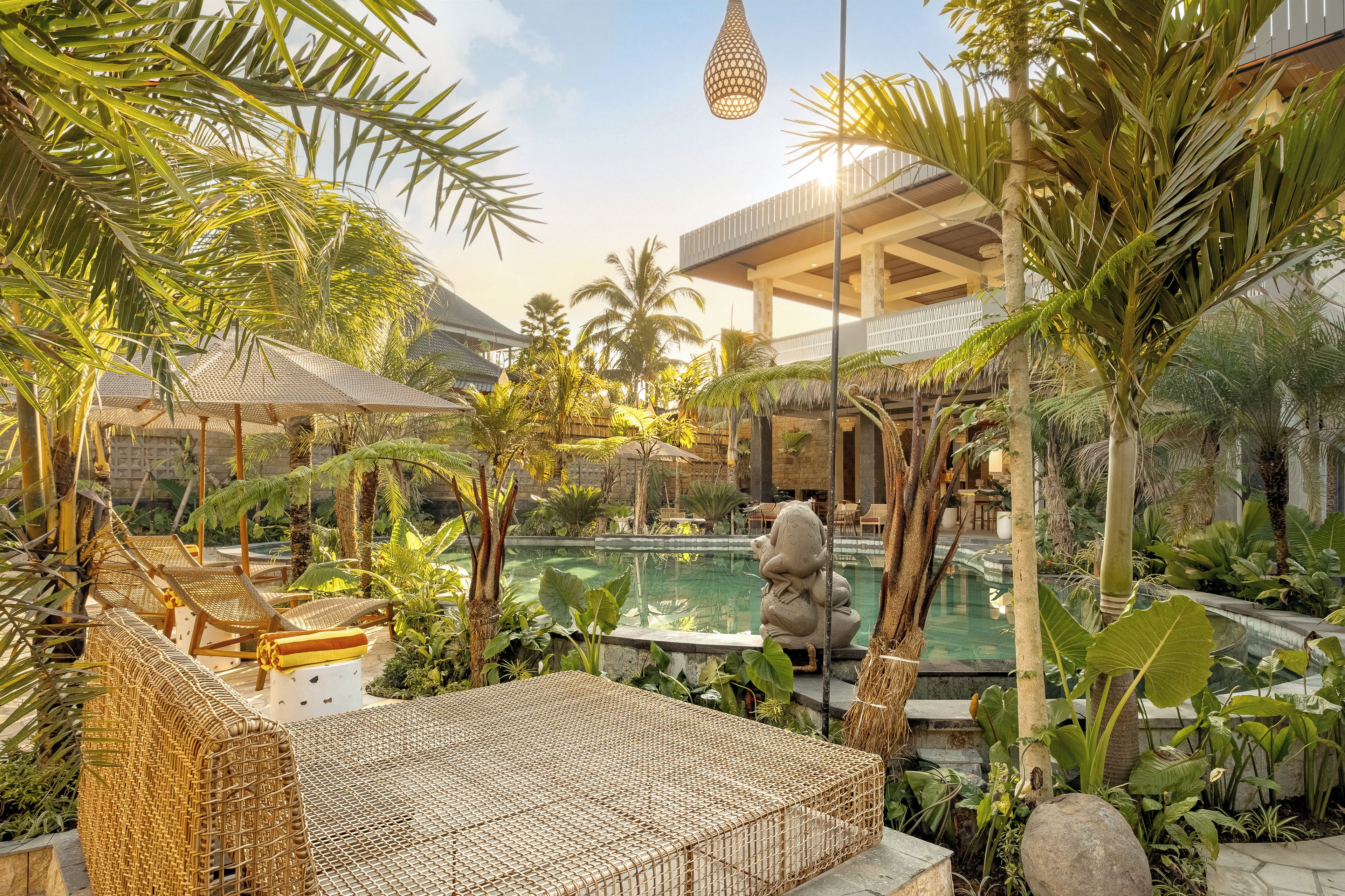 A pool area with lounge chairs, a stone statue, and tropical plants.