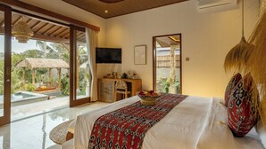 A bedroom with a bed, a television, a desk, and a view of a pool and outdoor area. - Dedari Sebatu Villa (Gianyar)