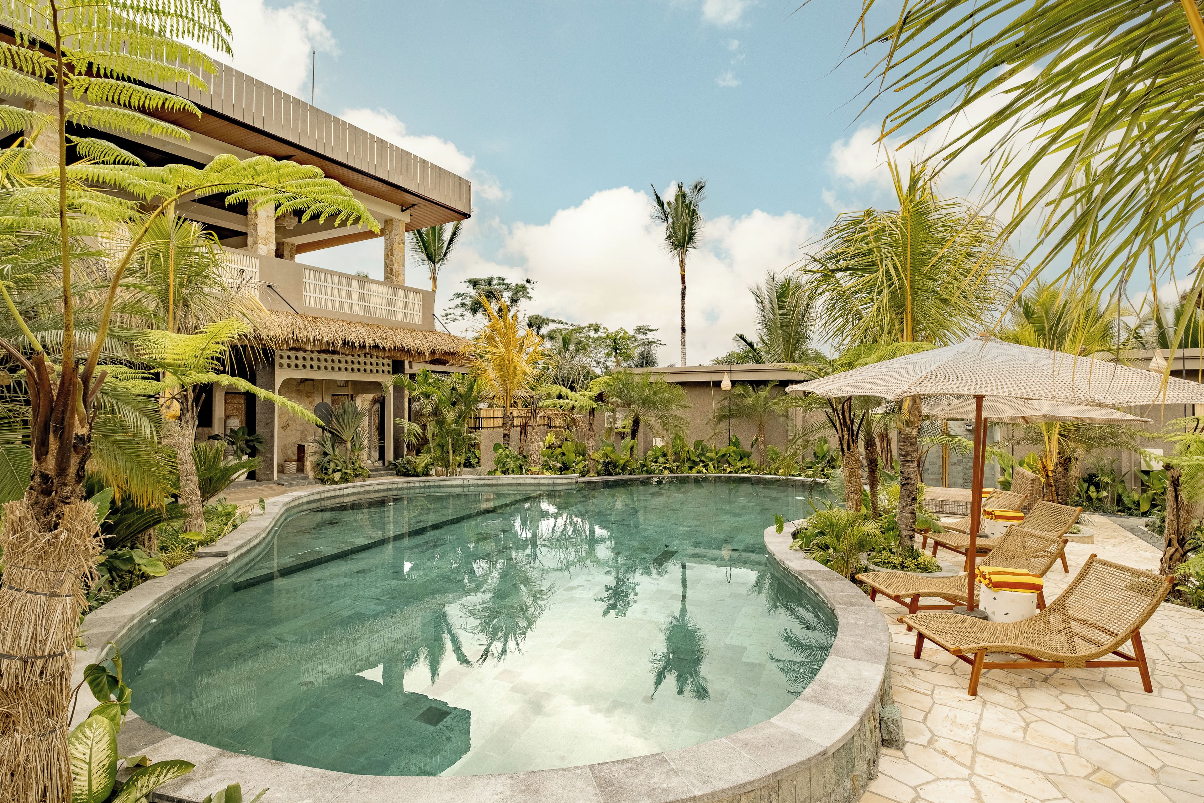 Una piscina rodeada de plantas tropicales y un edificio con balcón.