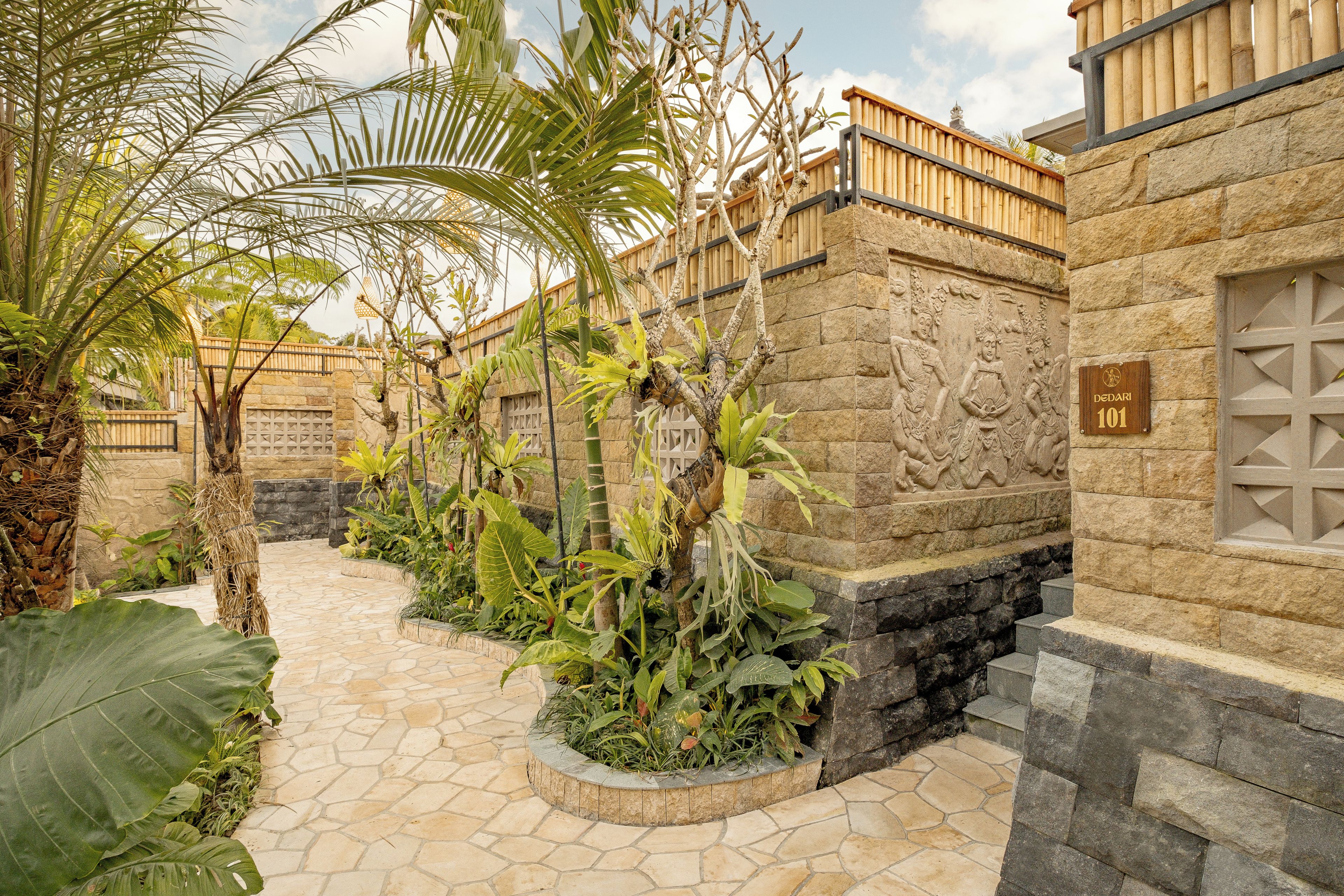 A stone pathway leading to a building with a wooden fence and a stone wall with carvings.