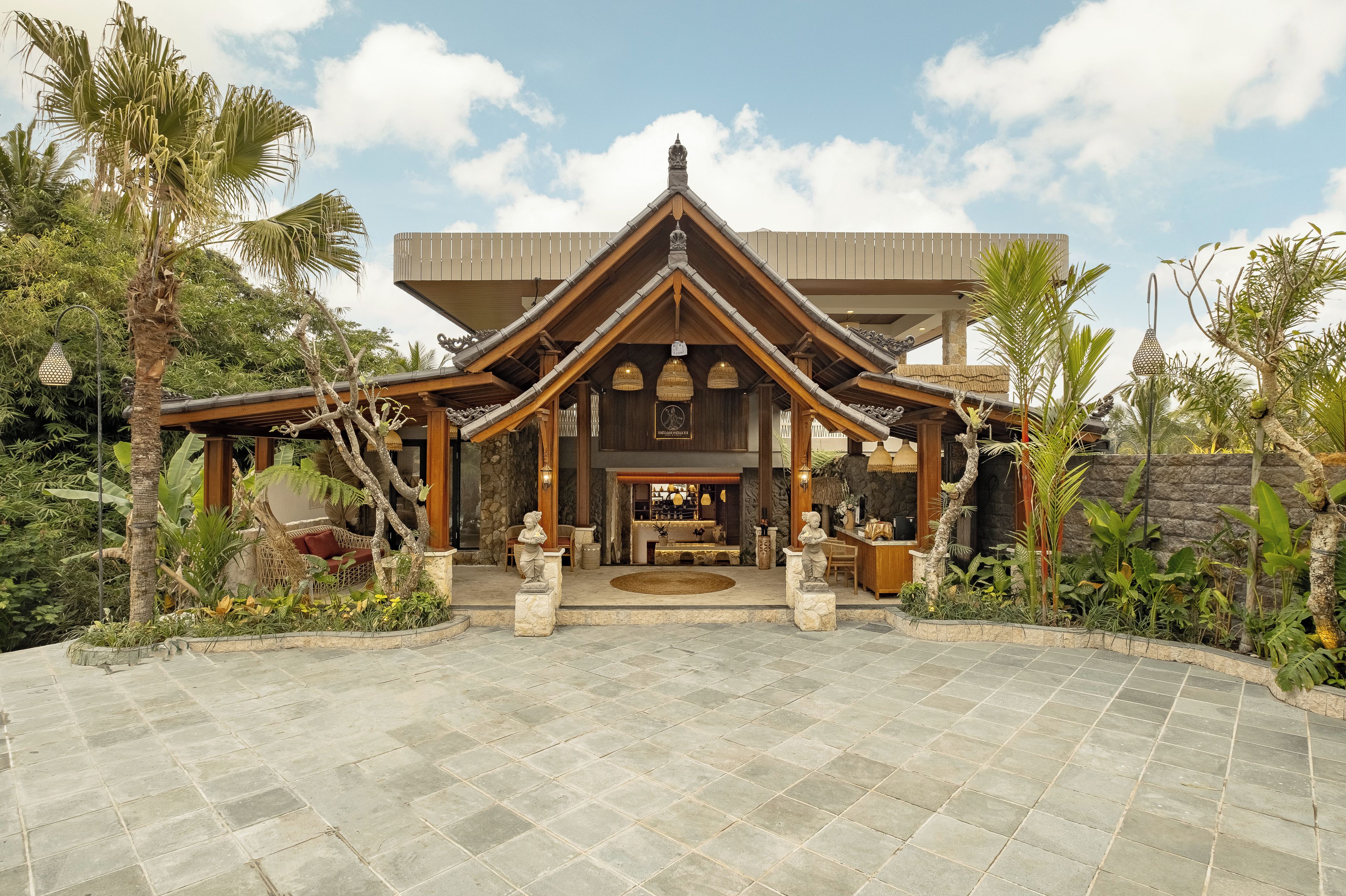 A traditional building with a central entrance, surrounded by stone tiles and tropical plants.