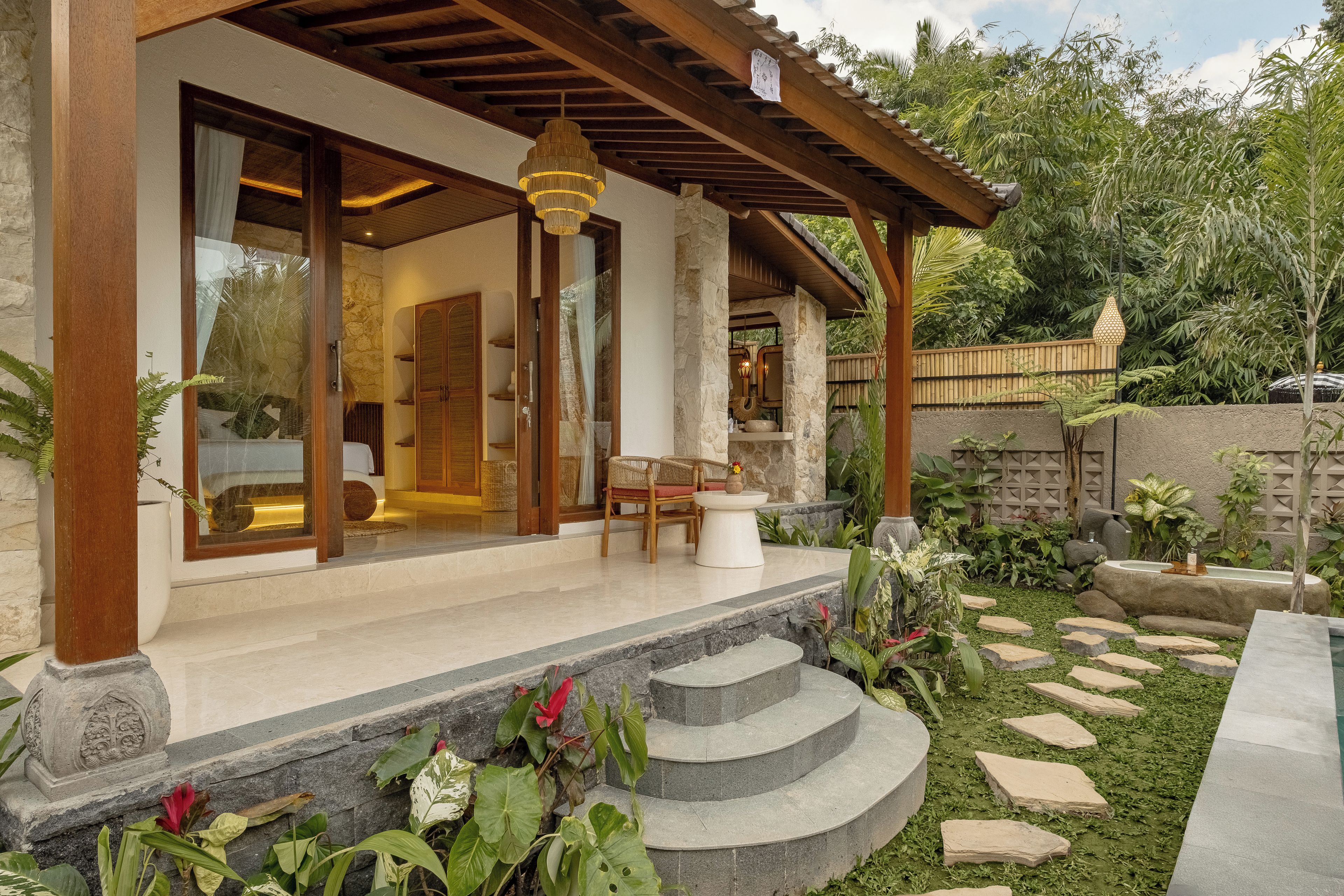 A covered outdoor area with a stone wall, a wooden pergola, and a seating area with a table and chairs.