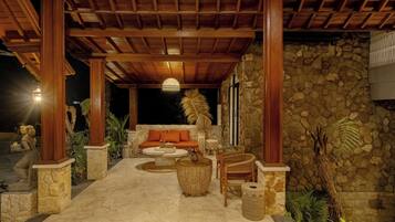 A covered outdoor seating area with stone pillars, a stone wall, and a hanging light fixture.