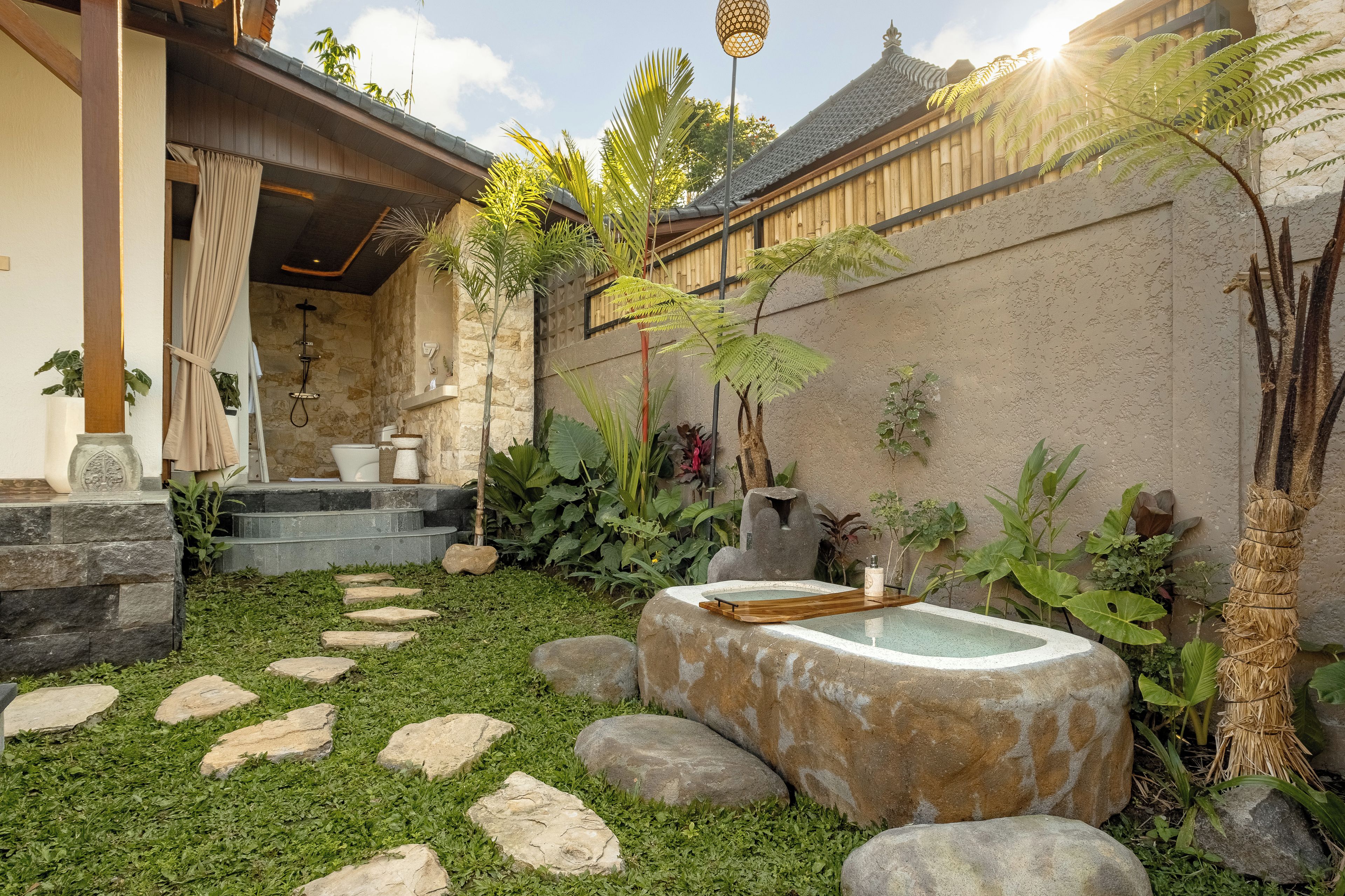 A stone-walled courtyard with a small water feature, stepping stones, and tropical plants.