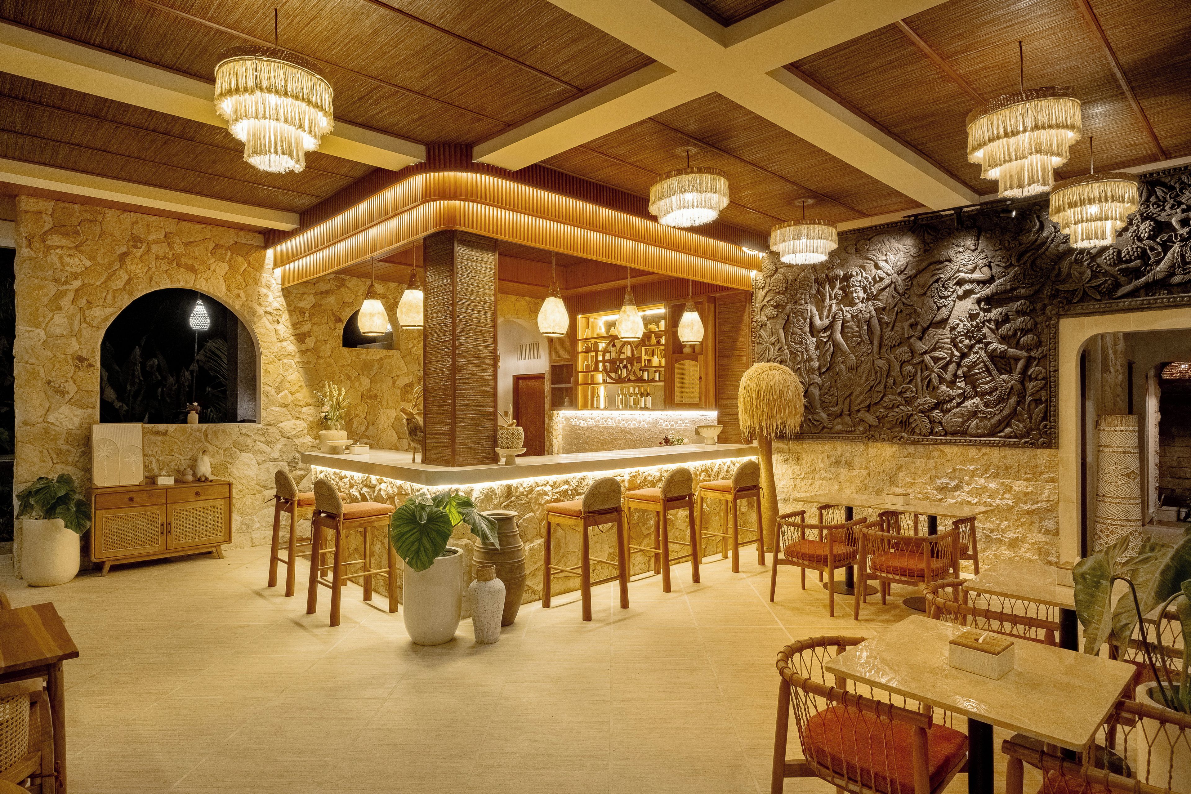 A restaurant interior with a bar area, stone walls, wooden ceiling beams, and hanging chandeliers.