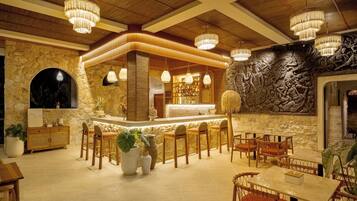 A restaurant interior with a bar area, stone walls, wooden ceiling beams, and hanging chandeliers.