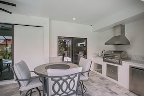 Eine Terrasse mit rundem Tisch und Stühlen, einem Grill und einer Glastür, die auf einen Balkon führt.