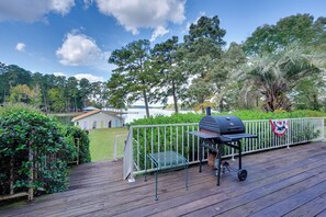 A wooden deck with a barbecue grill, a white fence, and a view of a lake and trees. - Luxury, 2 Master Suites, Fire Pit, Kayaks (Milledgeville)