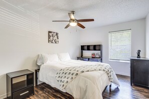 A bedroom with a bed, a nightstand, a desk, a ceiling fan, a window with blinds, and a wall-mounted picture. - Work, Explore & Unwind! Condo 2 Mi to UF (Gainesville)