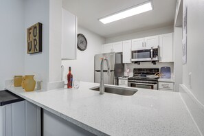 A modern kitchen with white cabinetry, stainless steel appliances, and a speckled countertop. - Work, Explore & Unwind! Condo 2 Mi to UF (Gainesville)