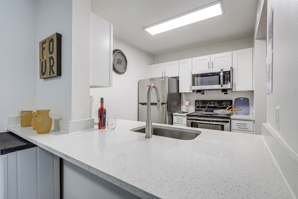 A modern kitchen with white cabinetry, stainless steel appliances, and a speckled countertop. - Work, Explore & Unwind! Condo 2 Mi to UF (Gainesville)