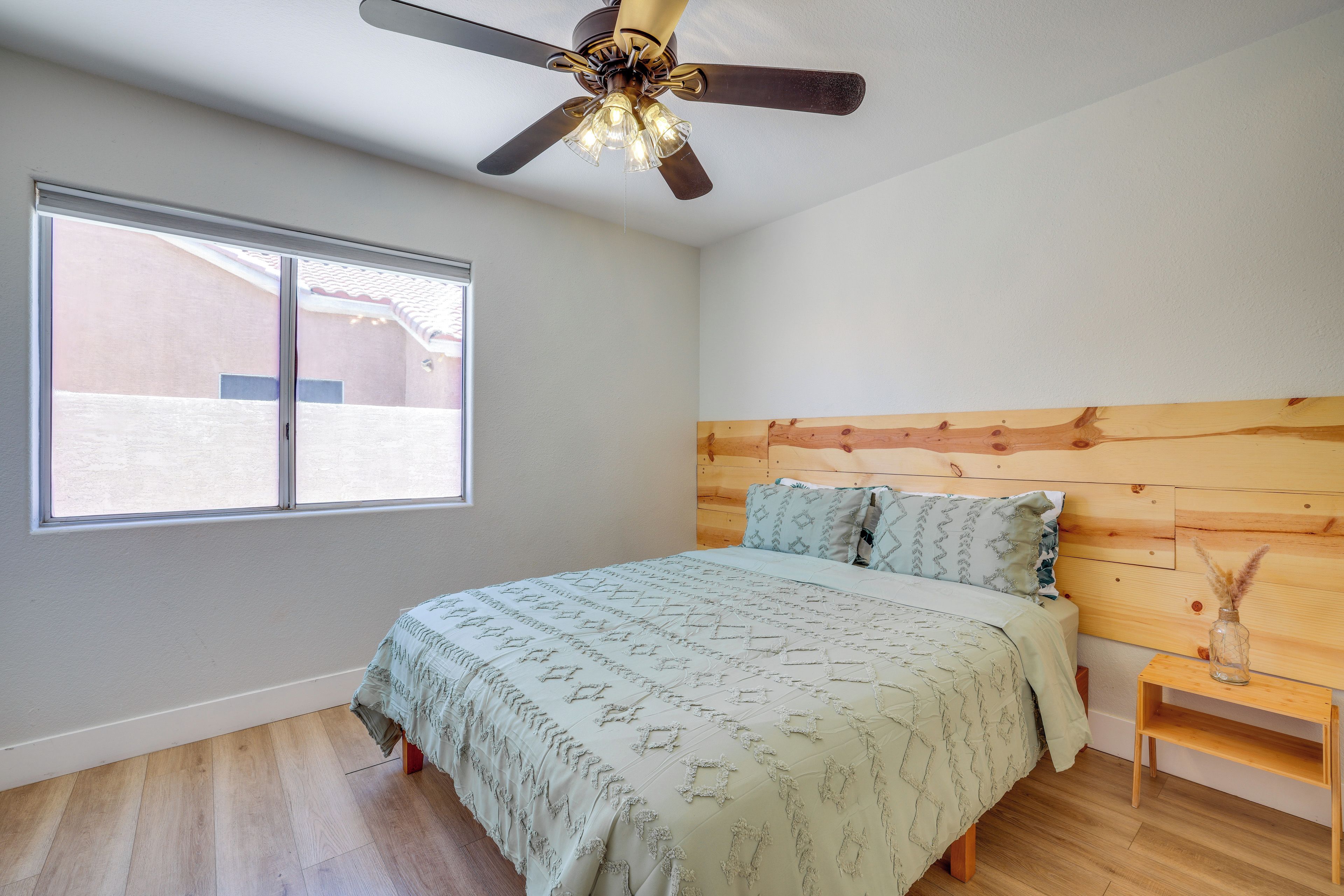 Un dormitorio con una cama, cabecera de madera, ventilador de techo y una ventana.