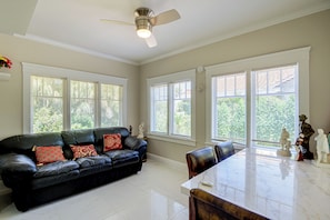 A spacious living room with a black leather sofa, a dining table, and a ceiling fan. - Hidden Gem Near Ocean Center, Water Park & Theater (Daytona Beach)