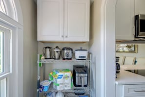 A kitchen with white cabinets, a coffee maker, a slow cooker, and a bag of paper towels. - Hidden Gem Near Ocean Center, Water Park & Theater (Daytona Beach)
