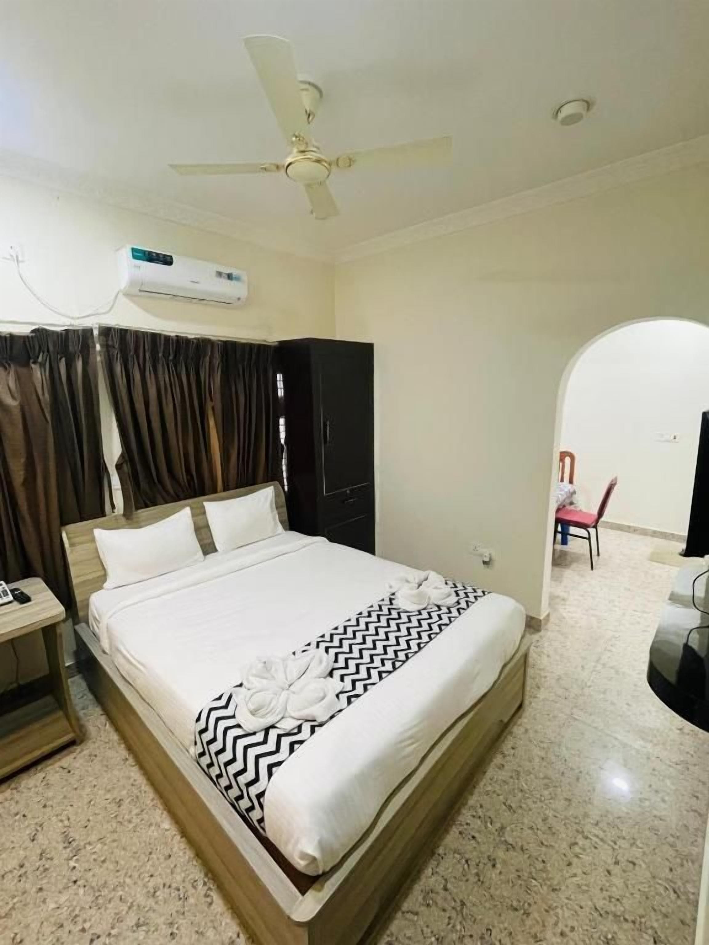 Een hotelkamer met een bed, een plafondventilator, een airconditioner, een kledingkast en een rode stoel.