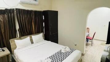 Een hotelkamer met een bed, een plafondventilator, een airconditioner, een kledingkast en een rode stoel.