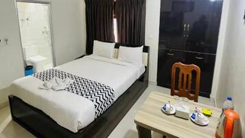 A hotel room with a bed, a desk, a chair, a ceiling fan, an air conditioning unit, a mirror, and a window with curtains.