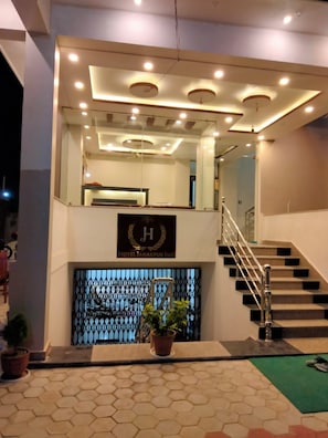 Zona de recepción de un hotel con una escalera, un mostrador de recepción y un cartel con el nombre del hotel.