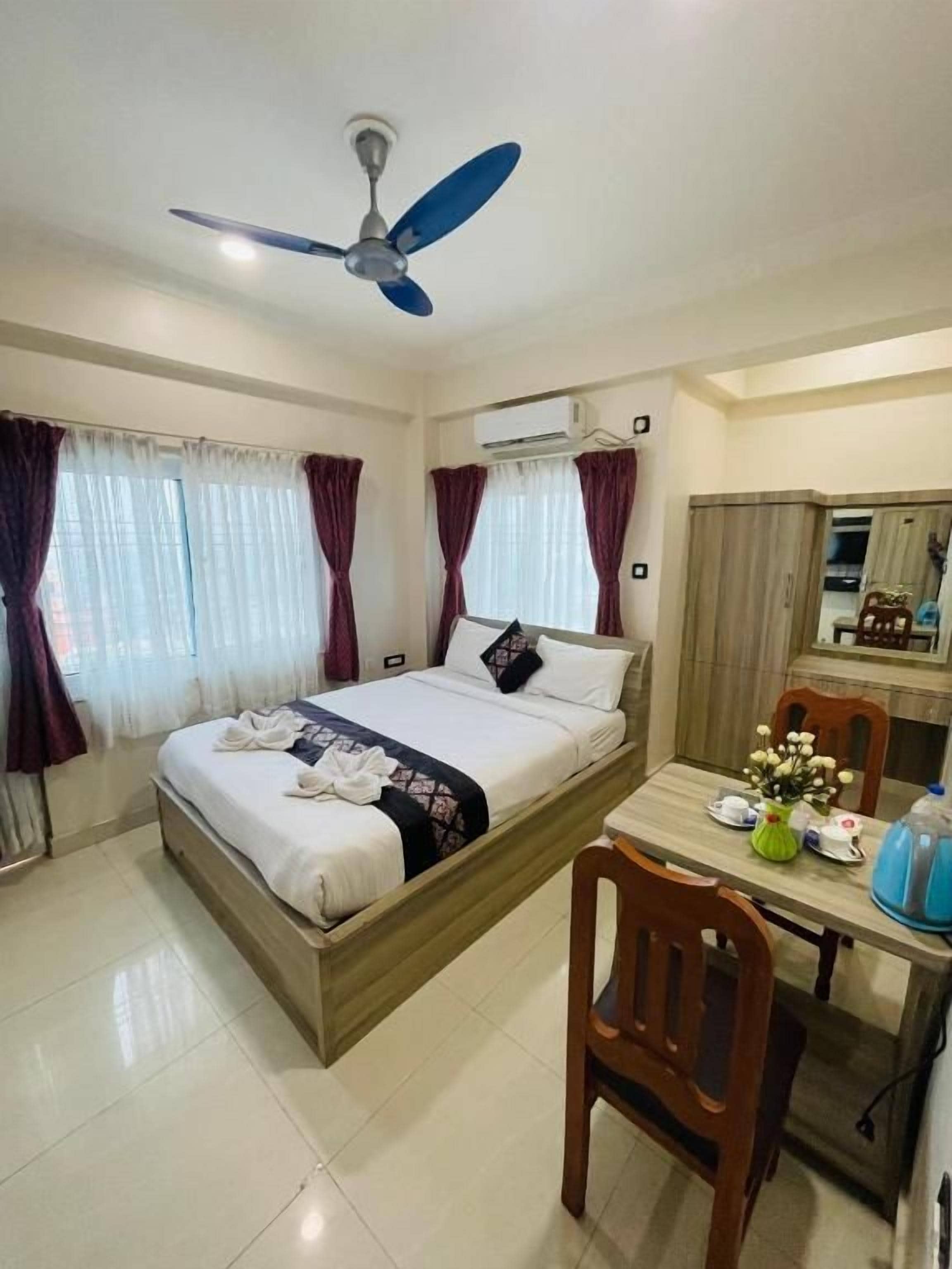 Una habitación de hotel con una cama, un escritorio, una silla, un ventilador de techo y cortinas.