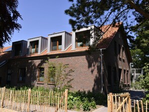 A brick building with a sloped roof and a wooden fence in the foreground. - Dream Crown Sky Blue (Schortens)