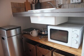 Una cocina compacta con un refrigerador de acero inoxidable, un horno microondas blanco y una tetera sobre una encimera de madera.