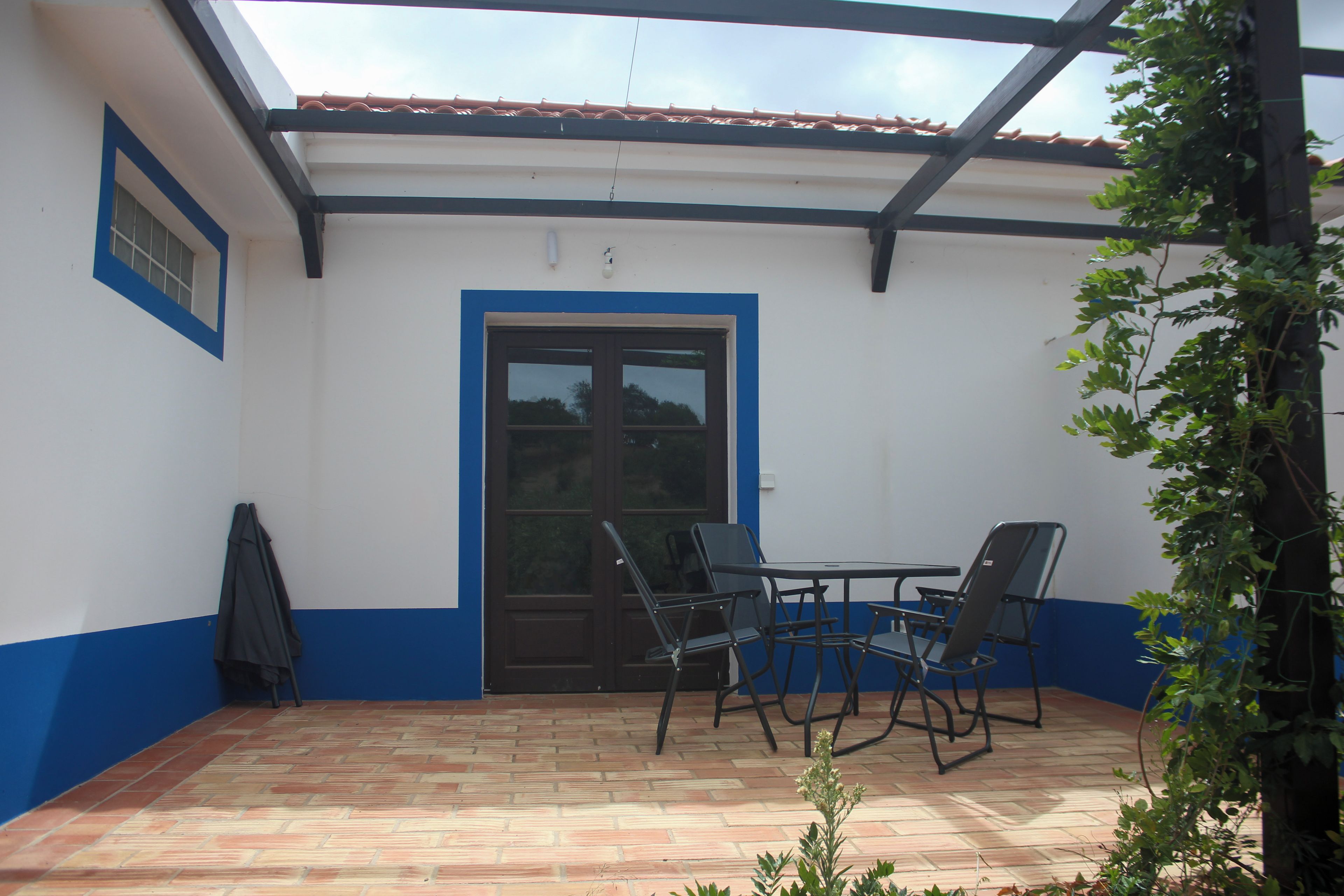 A covered patio with a table and chairs, a door, and a hanging plant.