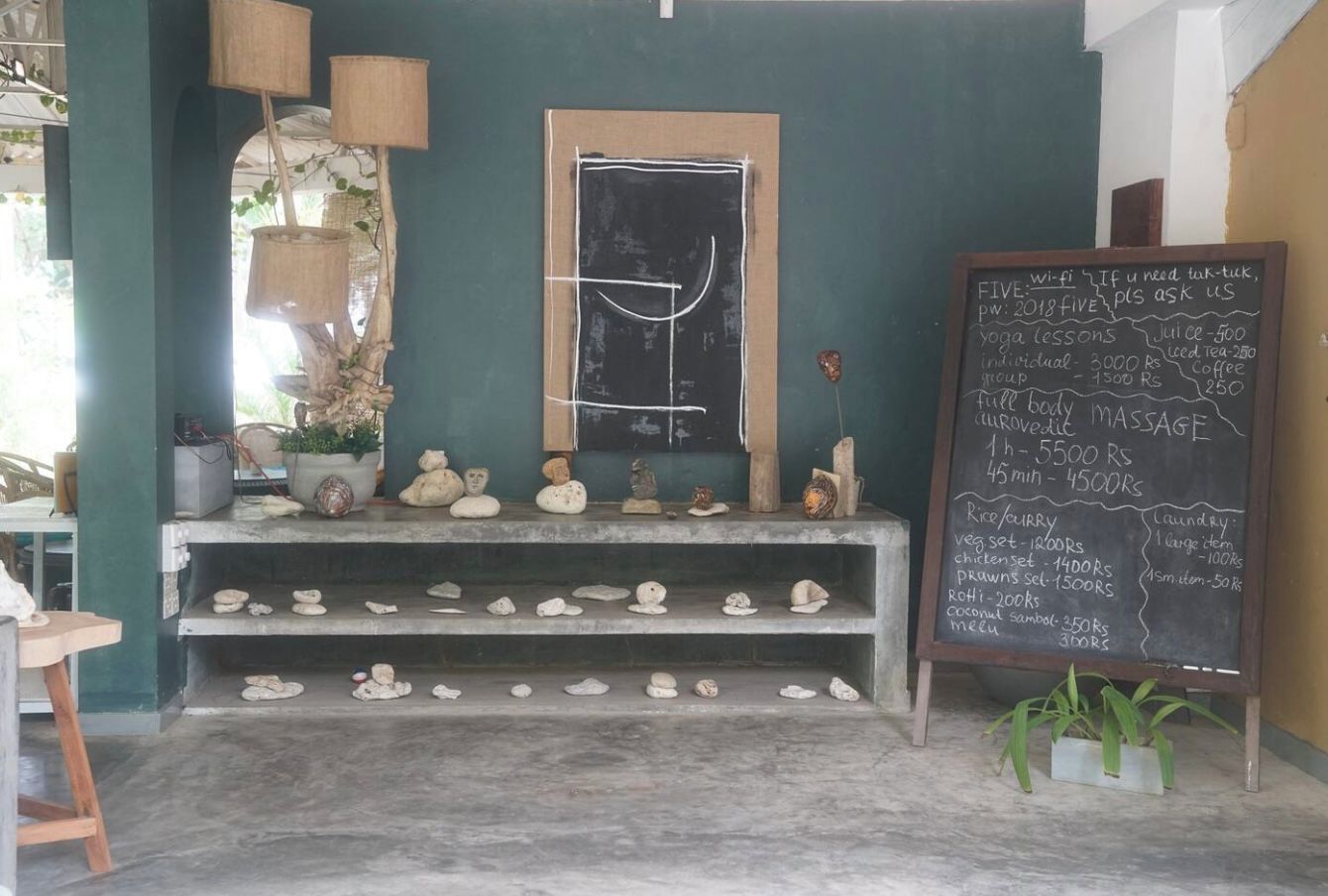 Quarto com lousa exibindo serviços e preços, prateleira com cerâmica e janela com vista.
