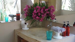 Un baño con lavamanos, espejo y un florero de flores rosadas.