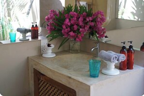 Et badeværelse med vask, spejl og en vase med lyserøde blomster.