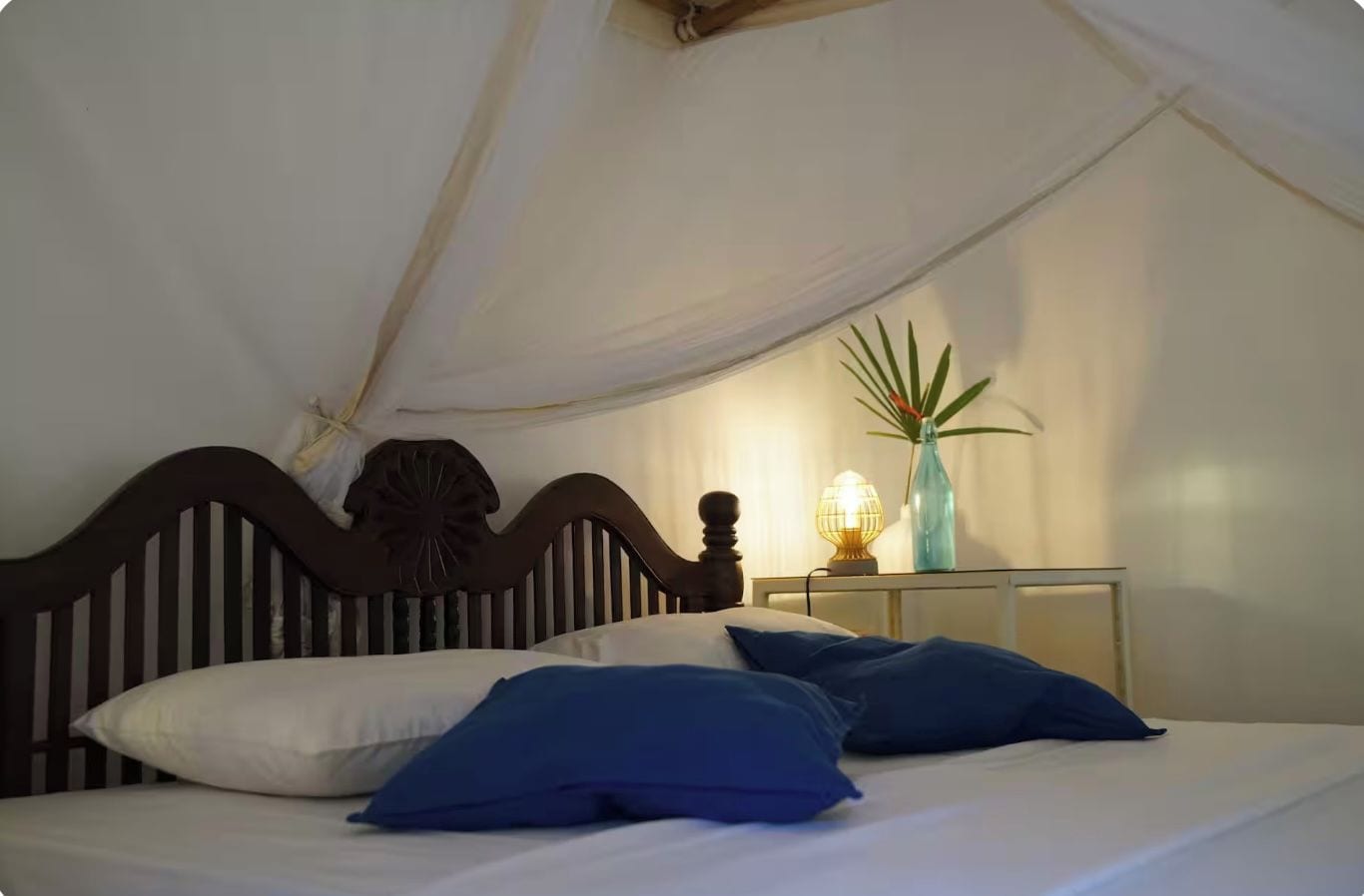 A bed with a canopy, a bedside lamp, and a potted plant.