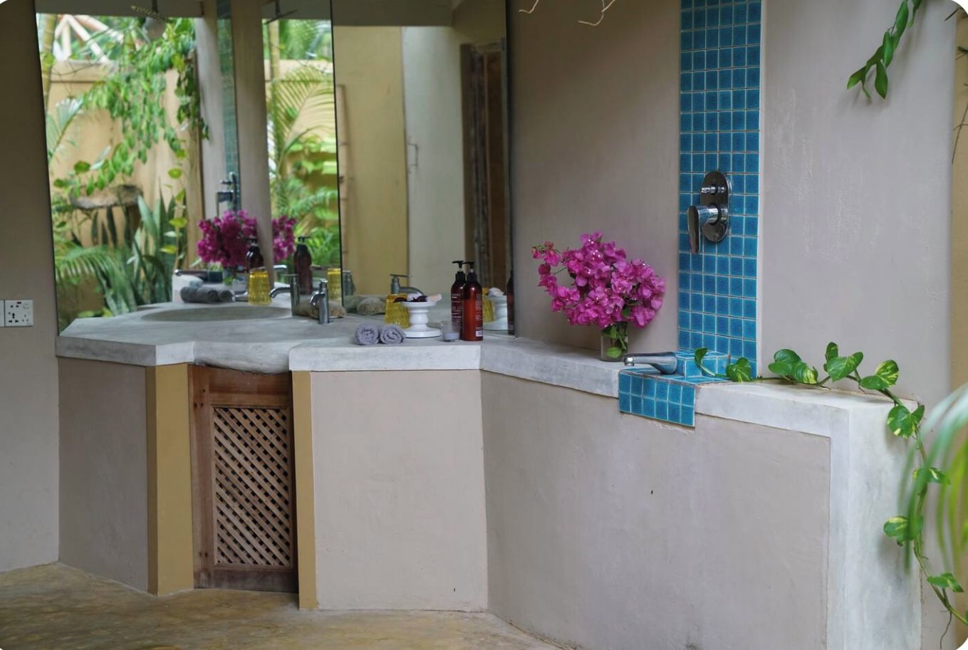 A bathroom with a curved vanity, a mirror, a sink, and a small window with blue tiles.