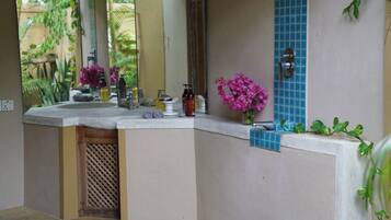 A bathroom with a curved vanity, a mirror, a sink, and a small window with blue tiles.
