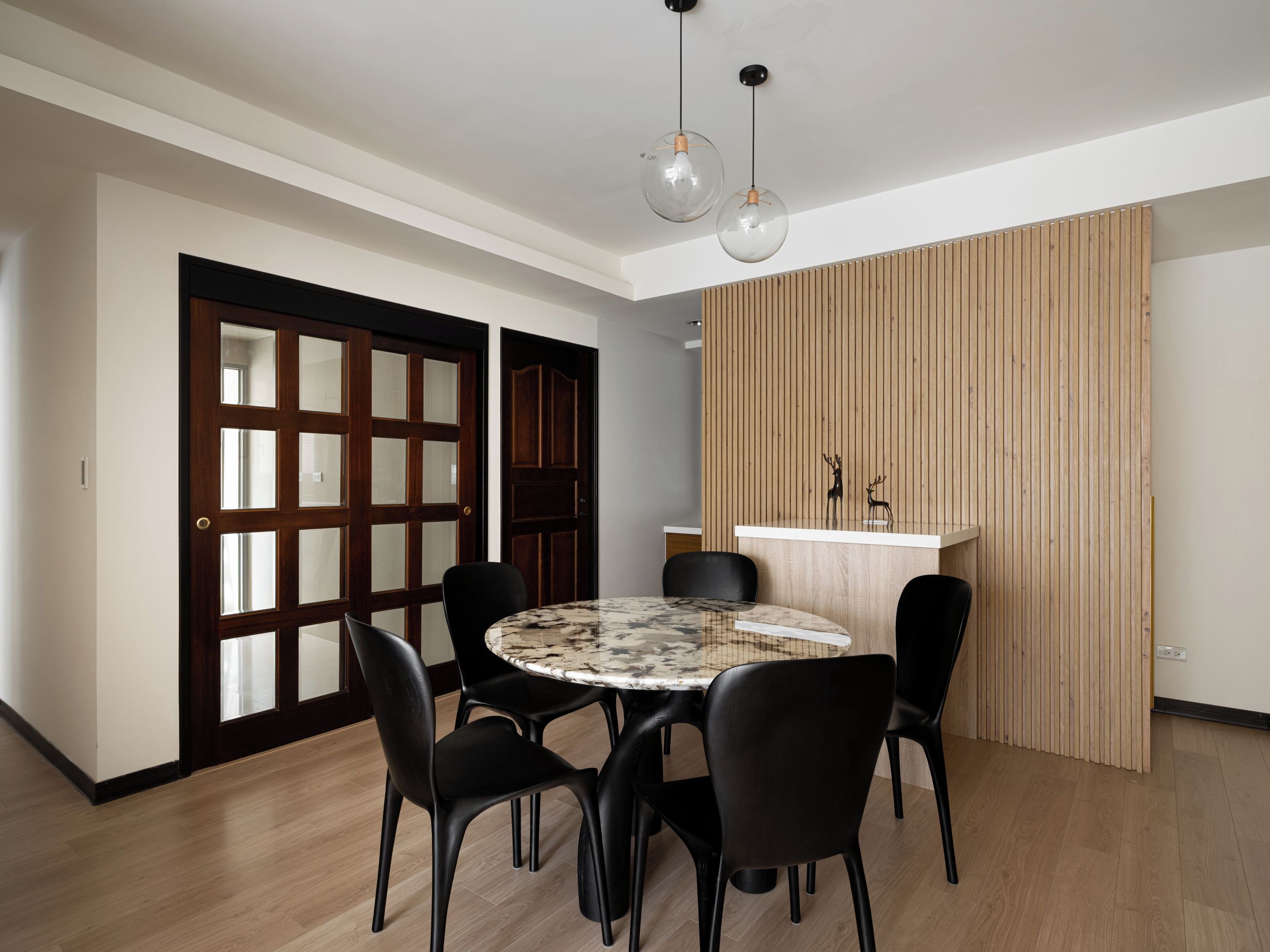 A dining area with a round table, black chairs, a wooden partition, and a wooden door.