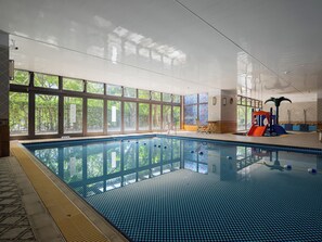 Ein Hallenbad mit großen Glaswänden, einer Rutsche und einer Sonnensegelkonstruktion.