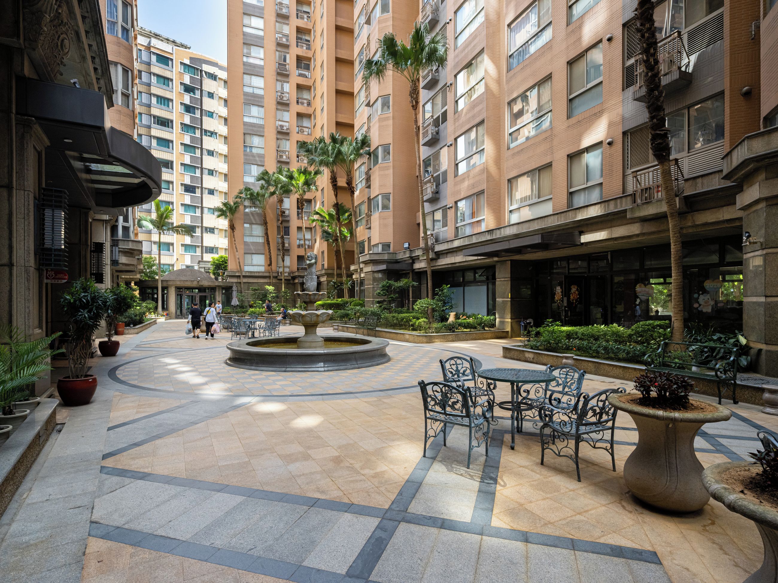 A courtyard with a fountain, seating areas, and tall residential buildings.