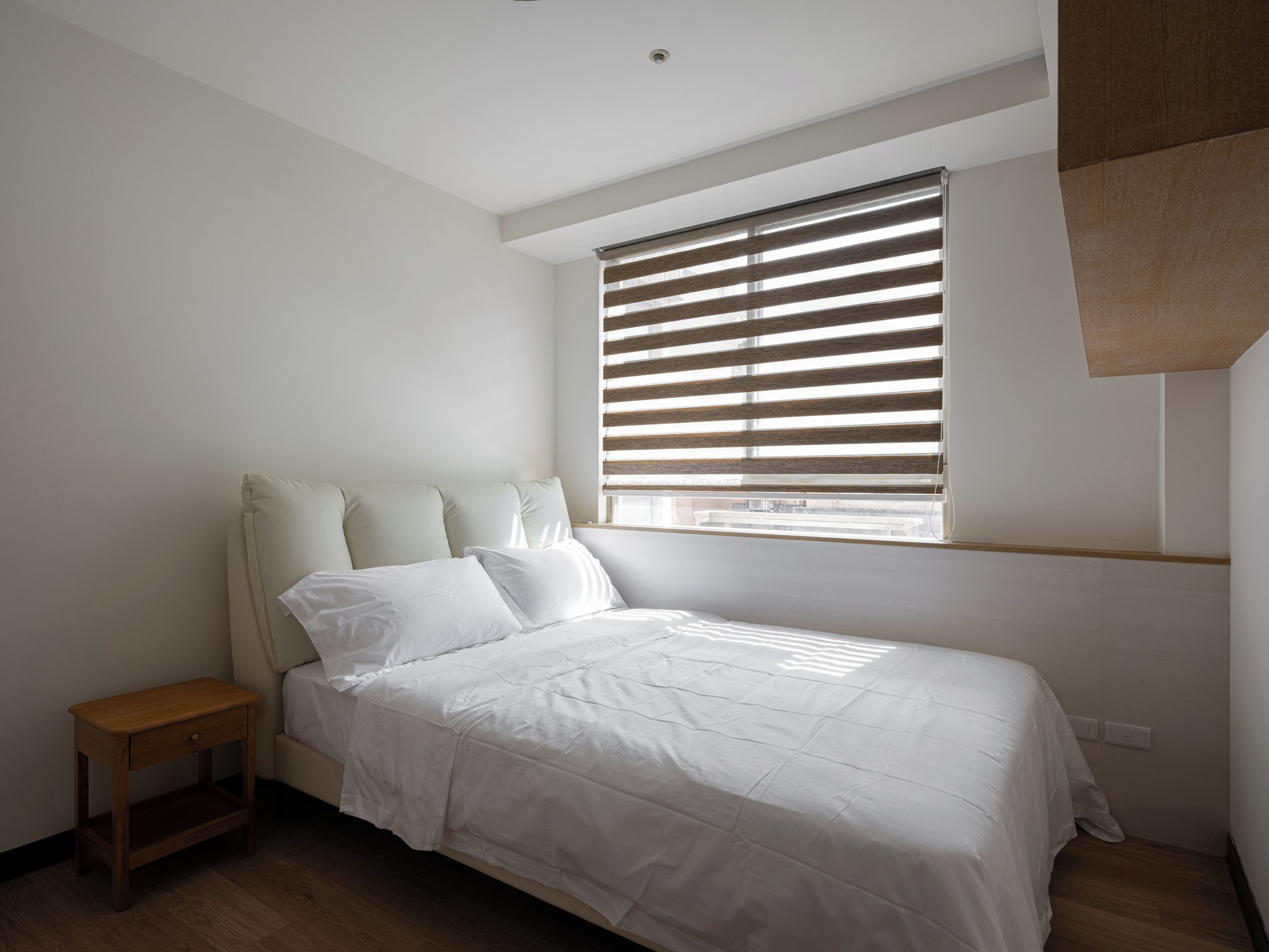 A bedroom with a bed, a nightstand, a window with blinds, and a sloped ceiling.