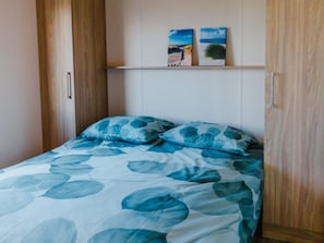 A bedroom with a bed, wooden wardrobe, and two wall-mounted pictures.