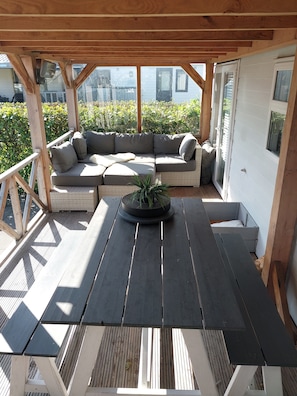 An outdoor seating area with a wooden table and benches, a cushioned sofa, and a potted plant.
