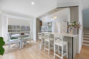 A modern kitchen with white cabinetry, a dining area with white chairs, and a view of the outdoors. - Spacious 3-bed Townhouse Near Broadwater (Gold Coast)
