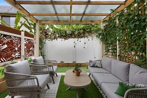 A covered patio with wicker furniture, a round table, and a white fence with climbing plants. - Spacious 3-bed Townhouse Near Broadwater (Gold Coast)