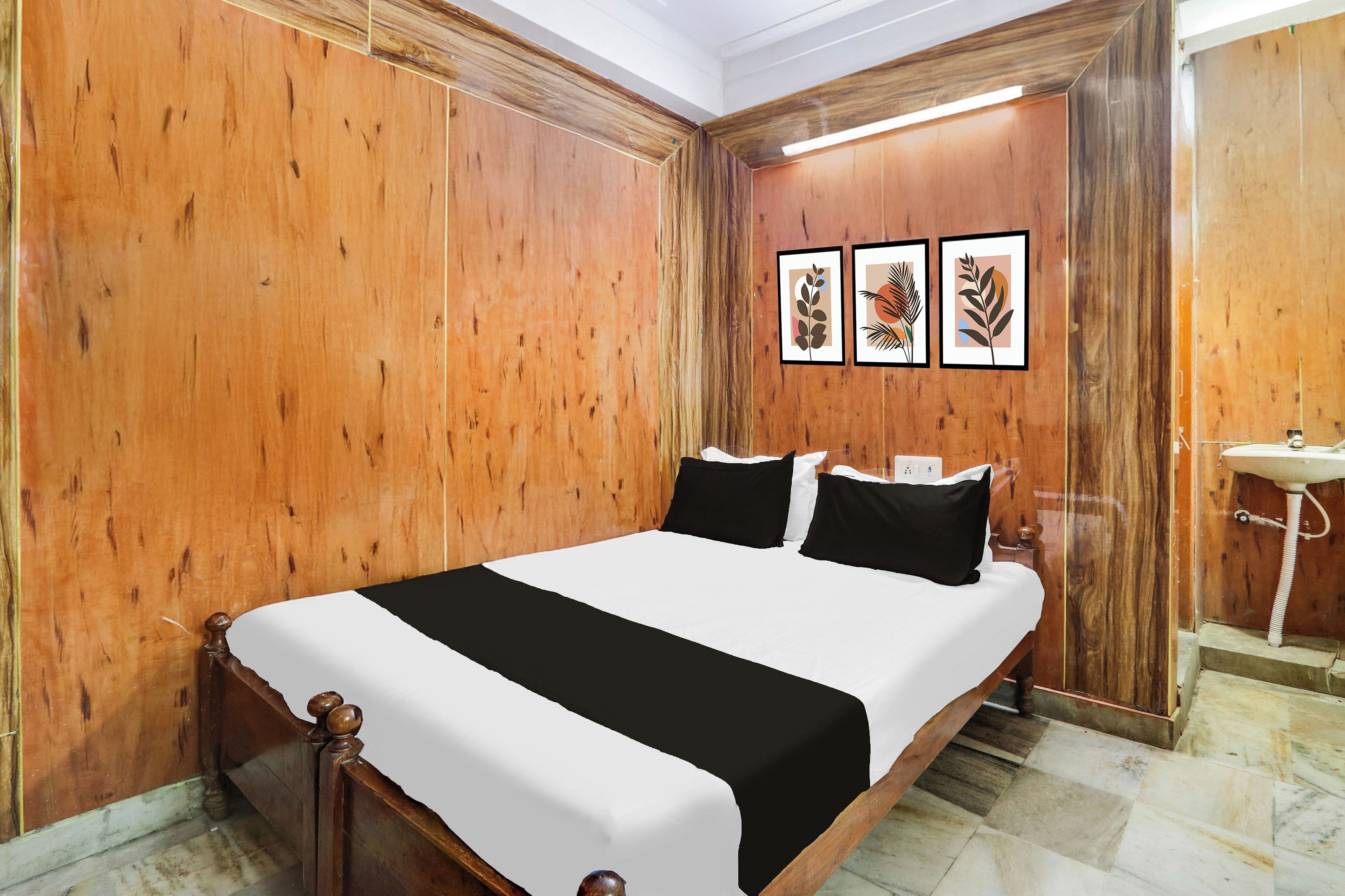 Habitación de hotel con pared de paneles de madera, cama con ropa de cama blanco y negro, y un baño pequeño con lavamanos.