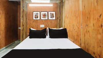 Quarto com cama, duas almofadas pretas, colcha branca e três impressões botânicas emolduradas na parede.